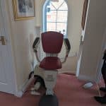 Flow 2a stairlift with red upholstered seat at the top of the stairs