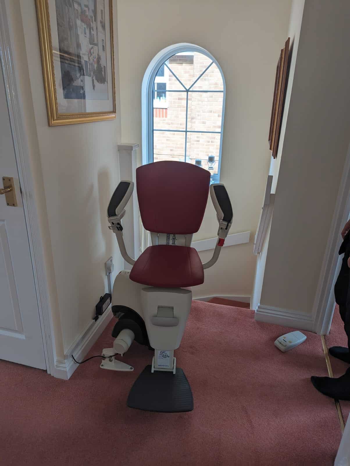 Flow 2a stairlift with red upholstered seat at the top of the stairs