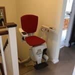Stairlift at the top of the stairs with red upholstered seat