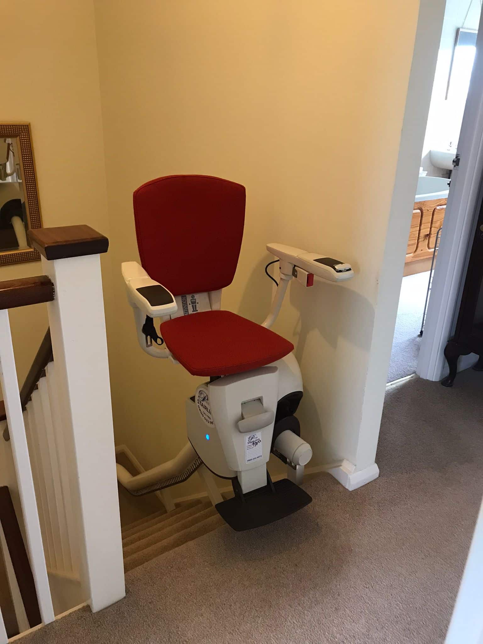 Stairlift at the top of the stairs with red upholstered seat