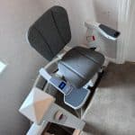 Stairlift with grey seat at the top of the stairs in ready position