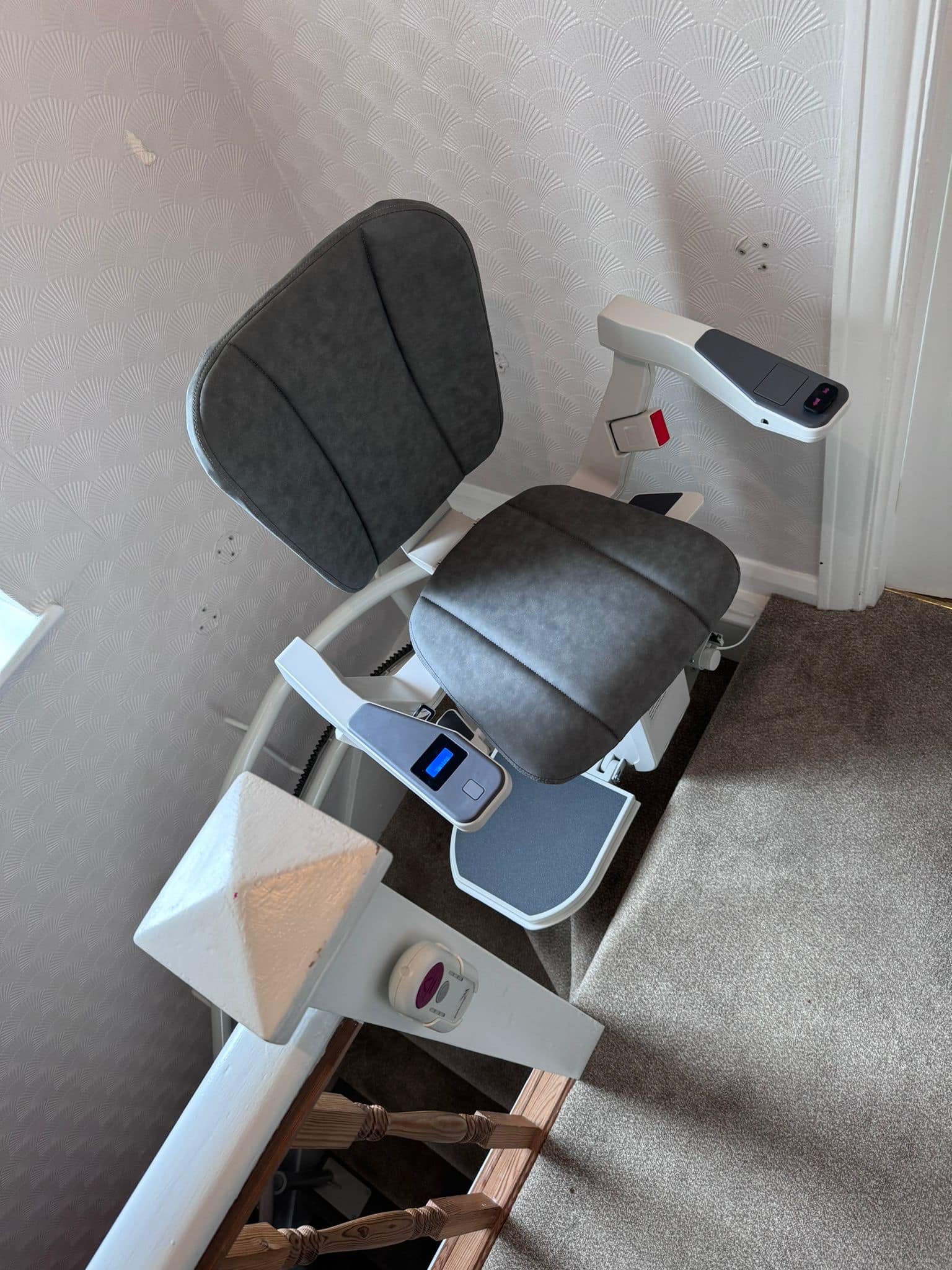 Stairlift with grey seat at the top of the stairs in ready position