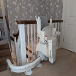 Otolift stairlift at the top of the stairs shown in its parked and folded position demonstrated from the side view