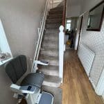 Platinum stairlift with grey upholstery at the bottom of the stairs in its ready position