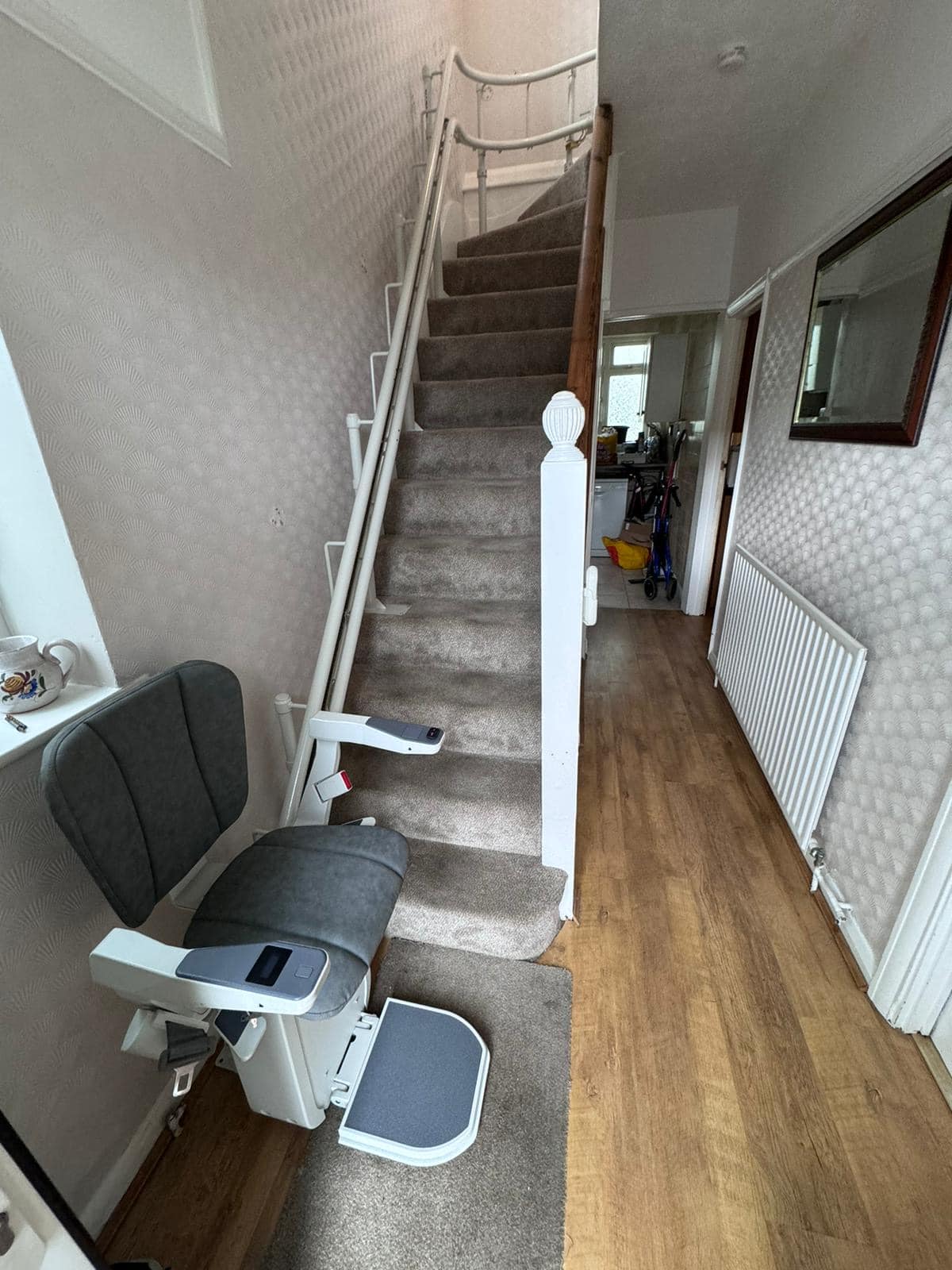Platinum stairlift with grey upholstery at the bottom of the stairs in its ready position