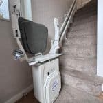 Platinum stairlift with grey upholstered seat in folded position at the bottom of the stairs