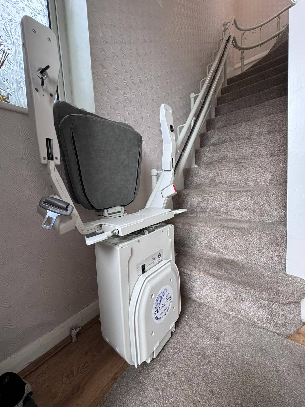 Platinum stairlift with grey upholstered seat in folded position at the bottom of the stairs