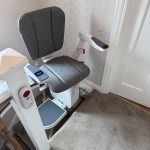 Stairlift with grey seat at the top of the stairs also showing remote control in holder attached to newel post