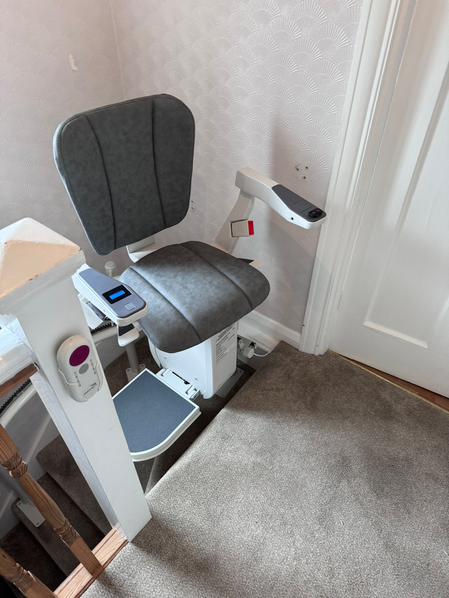 Stairlift with grey seat at the top of the stairs also showing remote control in holder attached to newel post