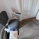 Stairlift with grey seat in ready position at the top of the stairs