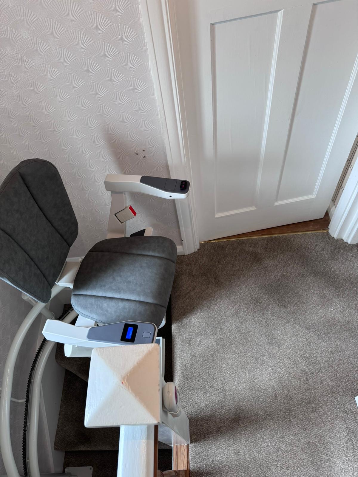 Stairlift with grey seat in ready position at the top of the stairs
