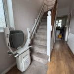 Stairlift with grey seat at the bottom of the stairs in folded position