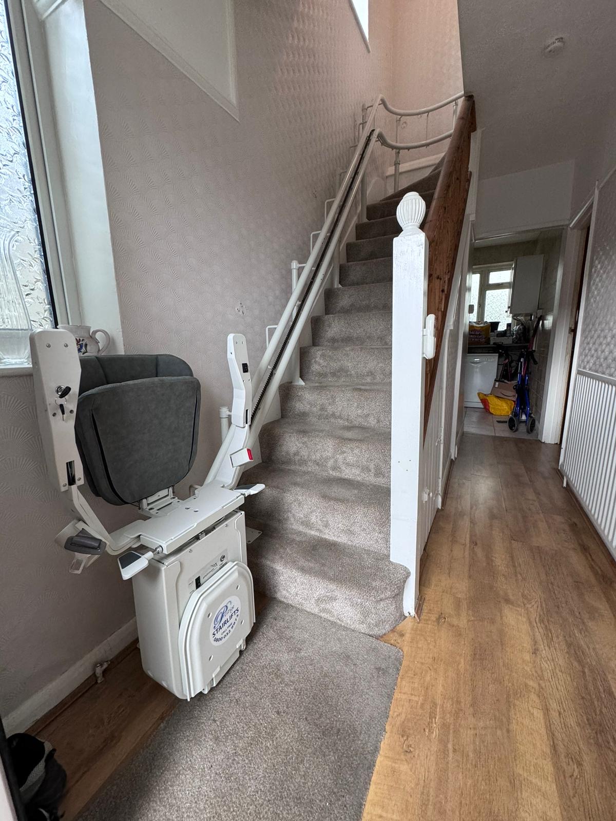 Stairlift with grey seat at the bottom of the stairs in folded position